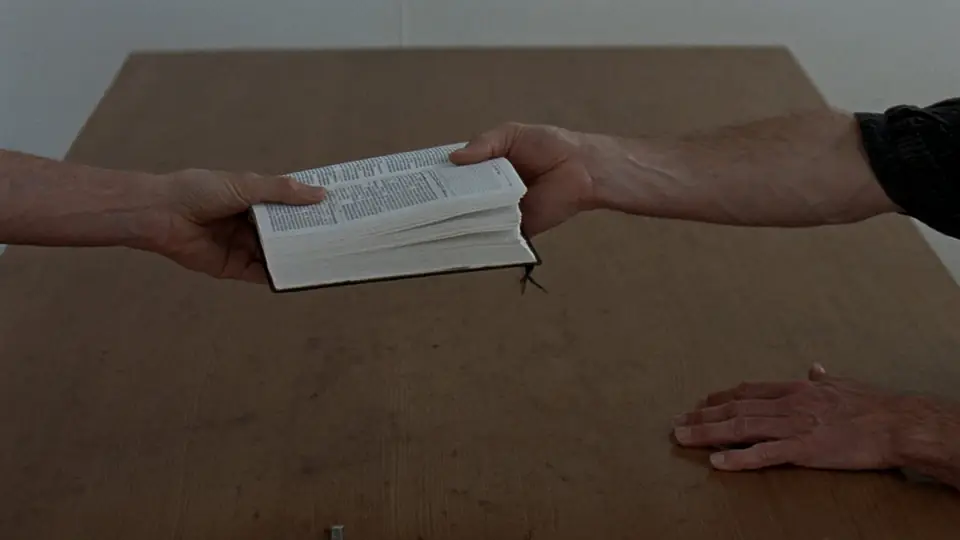 Dos personas se pasan una Biblia abierta sobre una mesa
