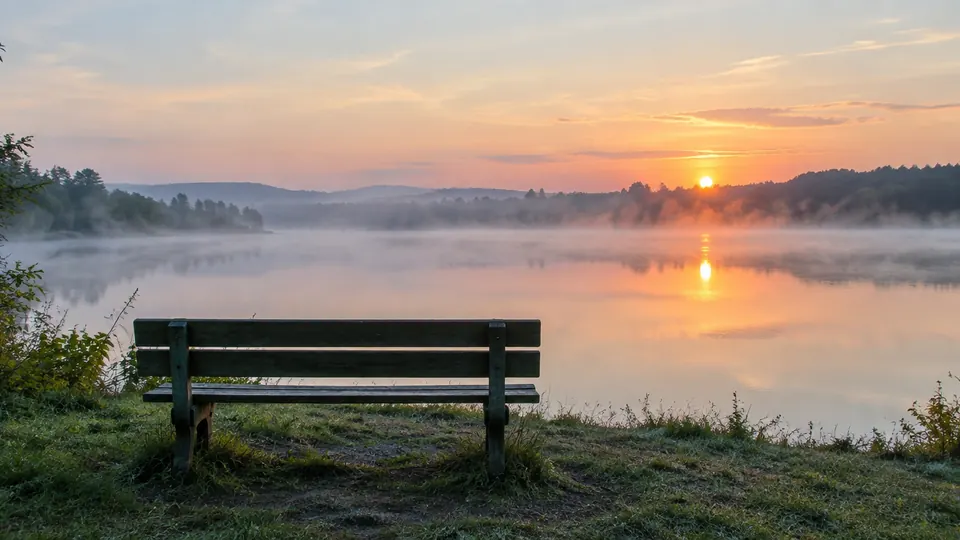 Banco de madera frente a un lago tranquilo al amanecer, con neblina suave