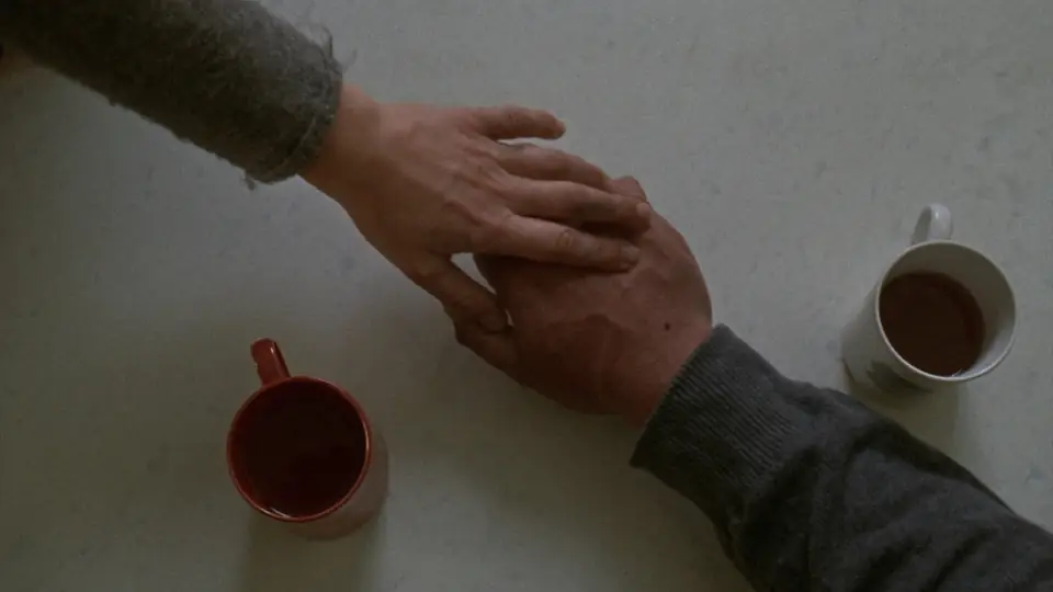 Una mano consuela a otra sobre una mesa de cocina, junto a dos tazas de té